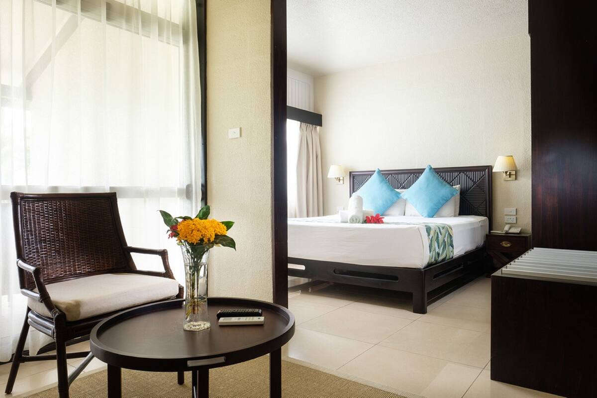 A hotel room with a bed, a chair, a table, and a vase of flowers.