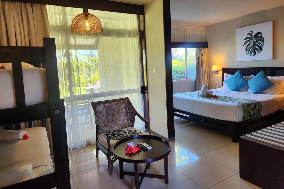 A hotel room with a bed, a chair, a small table, and a view of greenery outside.