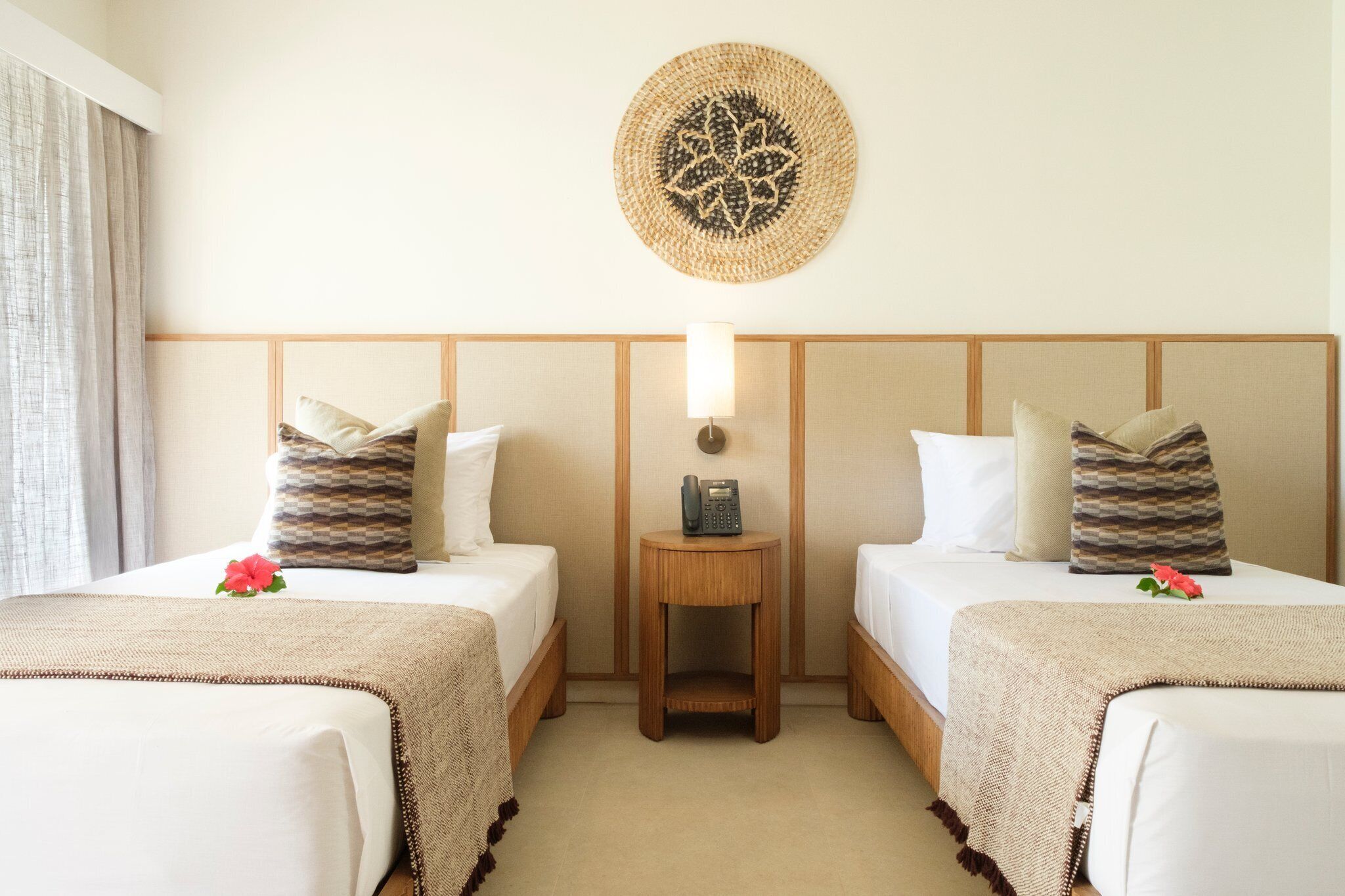 A hotel room with two beds, a bedside table with a lamp, and a decorative wall hanging.