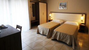 Quarto de hotel com duas camas de solteiro, uma escrivaninha, uma cadeira e um guarda-roupa.