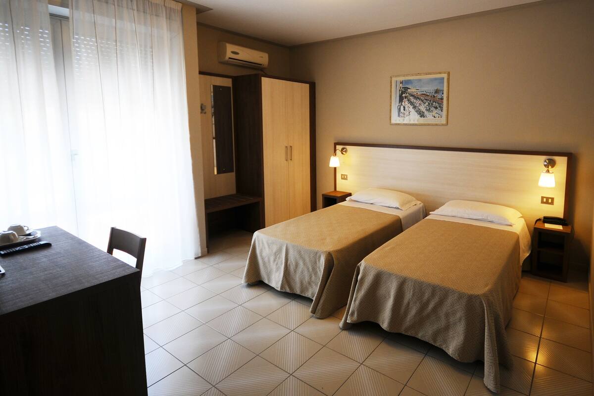 A hotel room with two single beds, a desk, a chair, and a wardrobe.