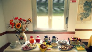 Uma mesa de pequeno-almoço com várias opções de comida, um vaso de flores e uma janela com persianas.