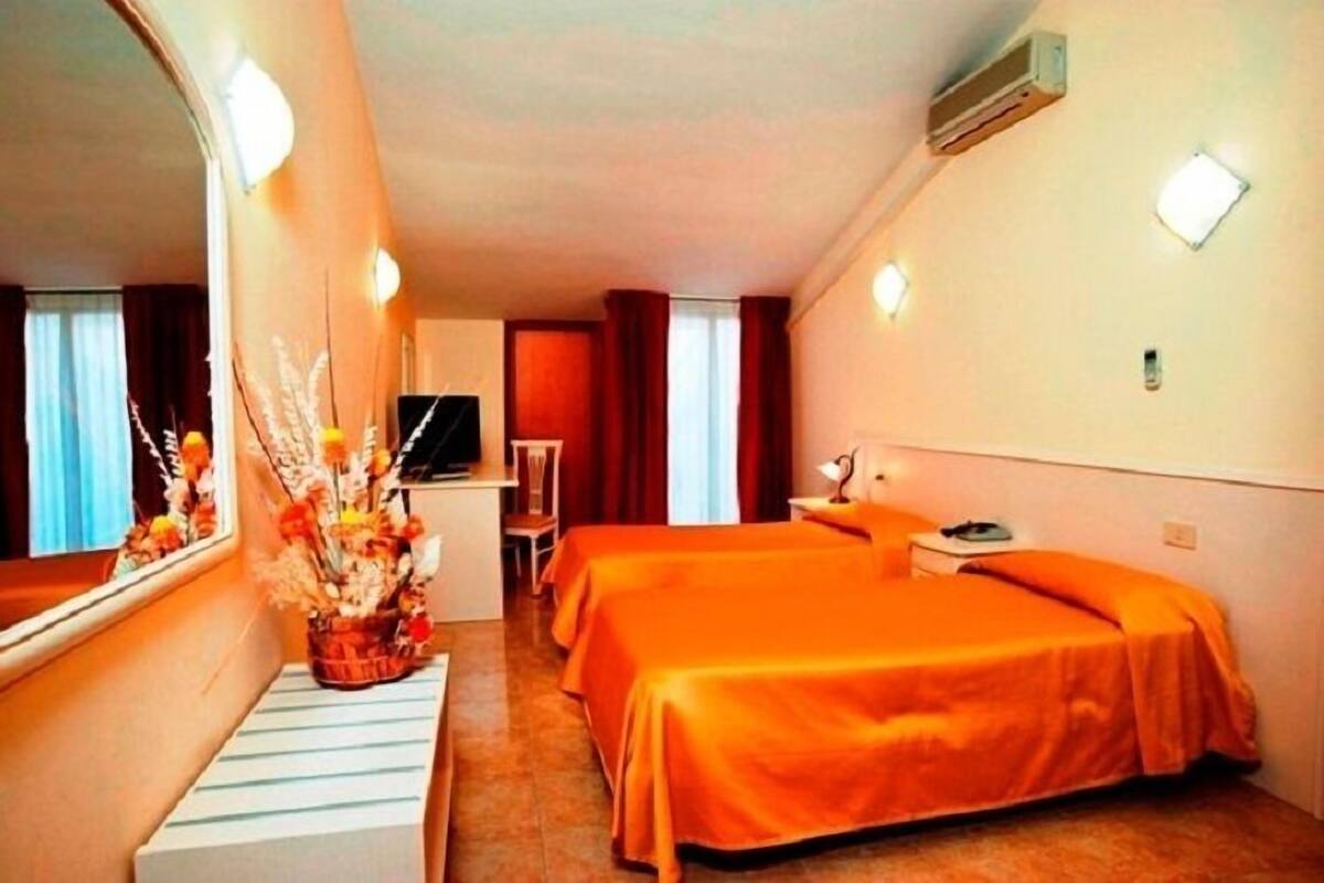 A hotel room with two beds, a desk, a chair, a TV, and a mirror.