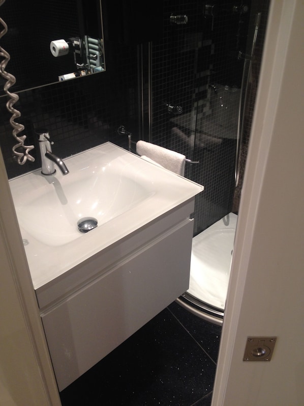 Un baño con lavamanos blanco, un espejo y zona de ducha.