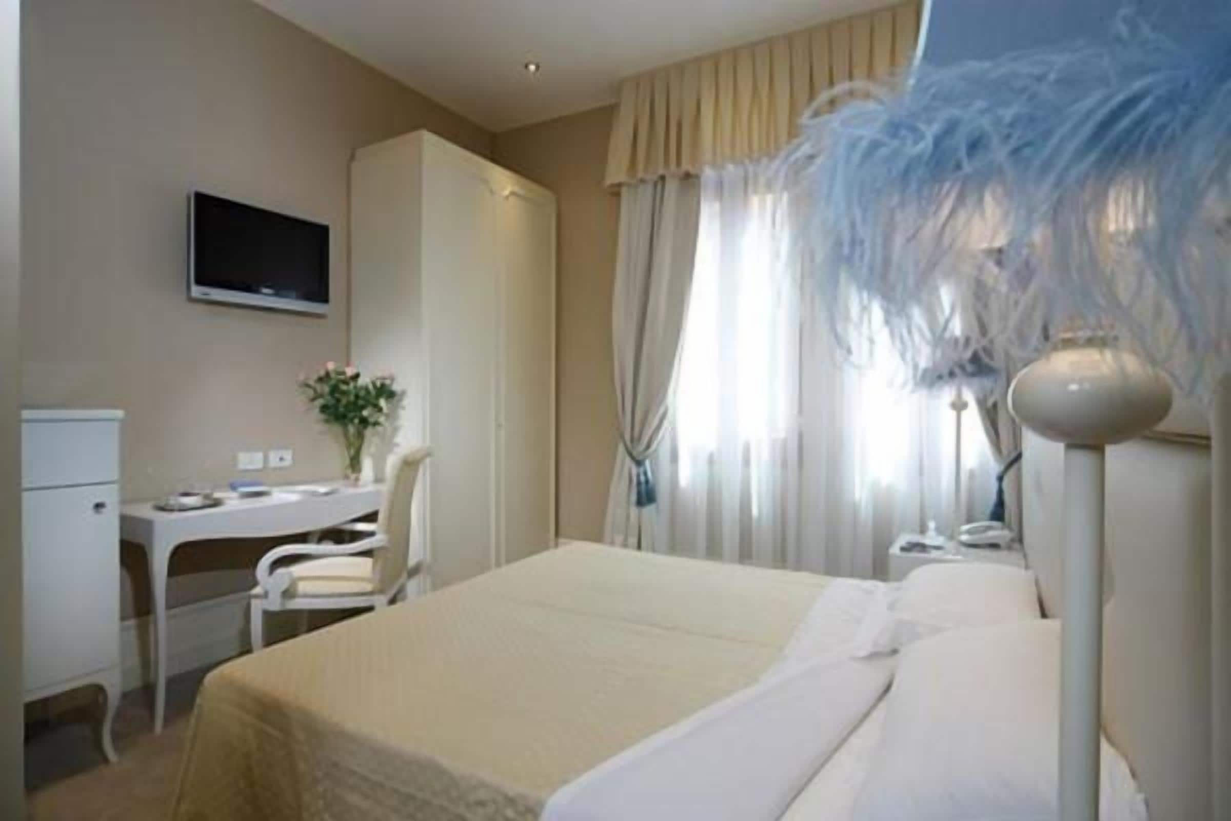 Une chambre d’hôtel équipée d’un lit, d’un bureau, d’une chaise, d’une télévision et de rideaux.