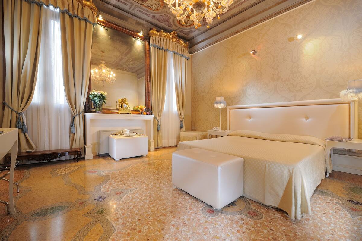 Um quarto luxuoso com uma cama grande, mesa de cabeceira, espelho e lustre.