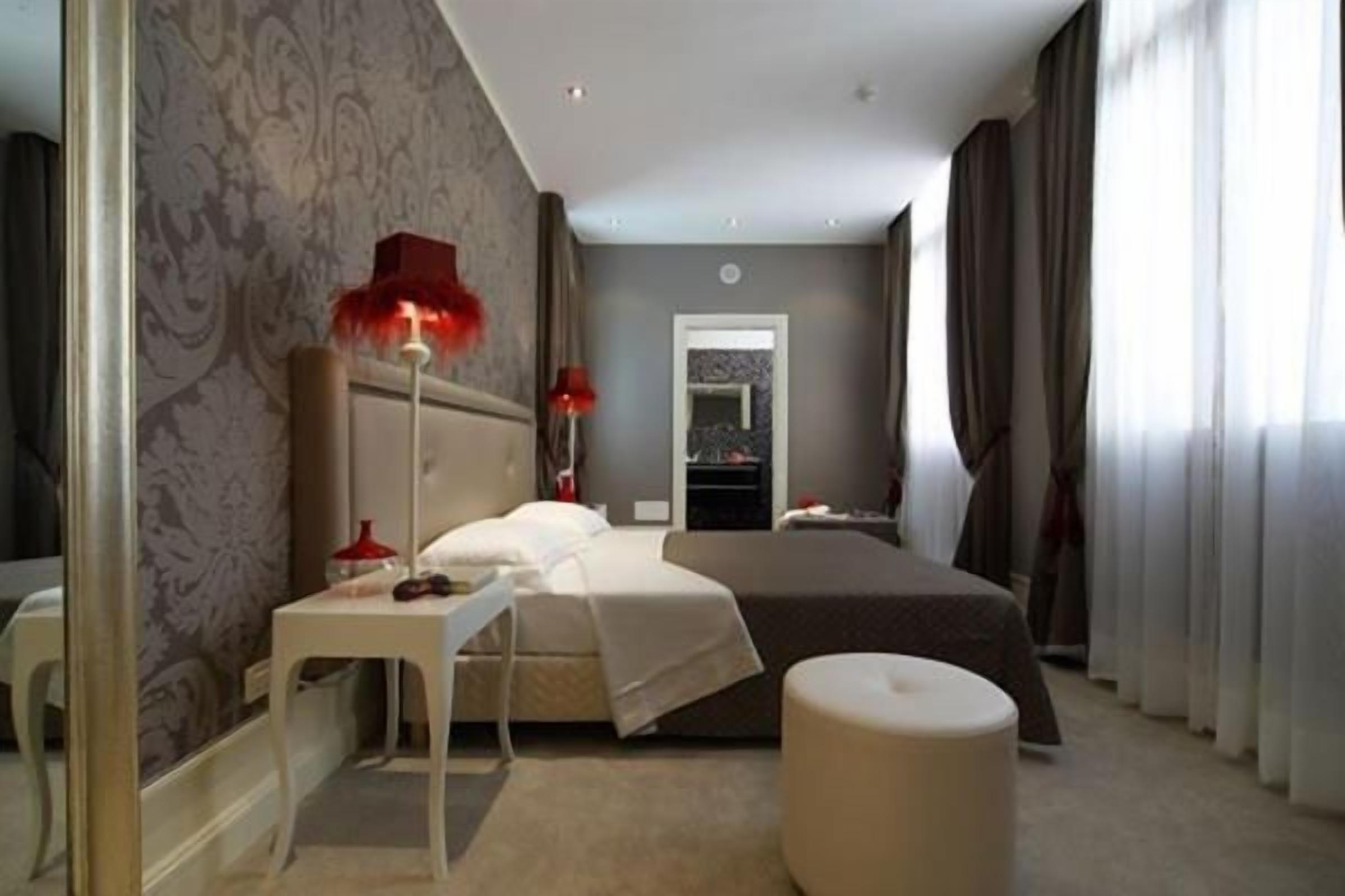 Una camera d'albergo con un letto, comodino, lampada e vista sulla città dalla finestra.