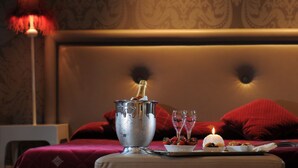 A bed with red pillows, a bedside table with a champagne bottle, glasses, and strawberries. - Hotel Ai Due Principi (Venice)