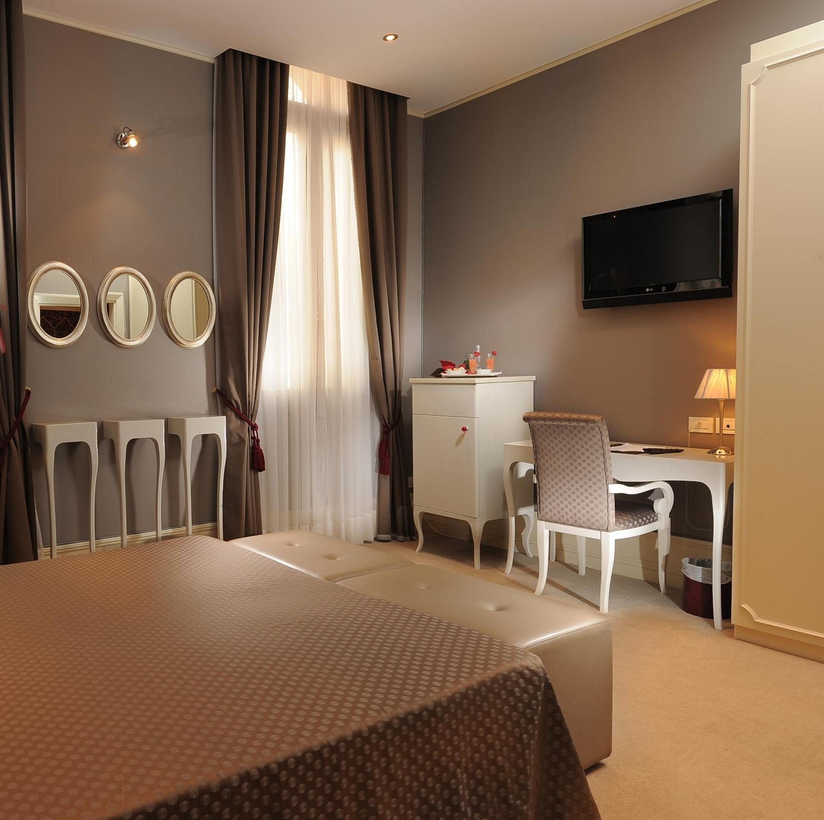 A hotel room with a bed, a desk, a chair, a television, and three mirrors.