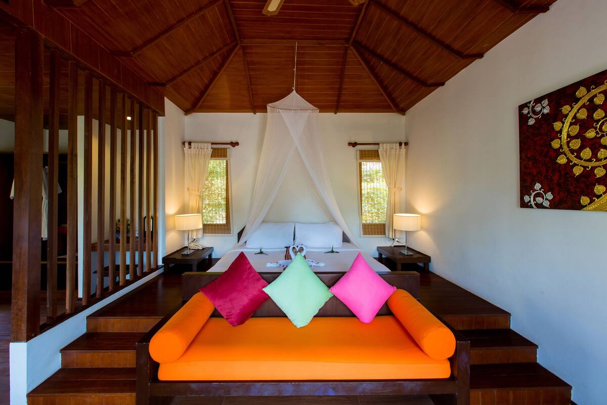 Un dormitorio con una escalera de madera, una cama con dosel y un sofá naranja brillante.