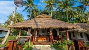 A thatched-roof bar area with wooden furniture and a 'Welcome' sign, surrounded by palm trees. - Elixir Koh Yao Yai (Ko Yao)