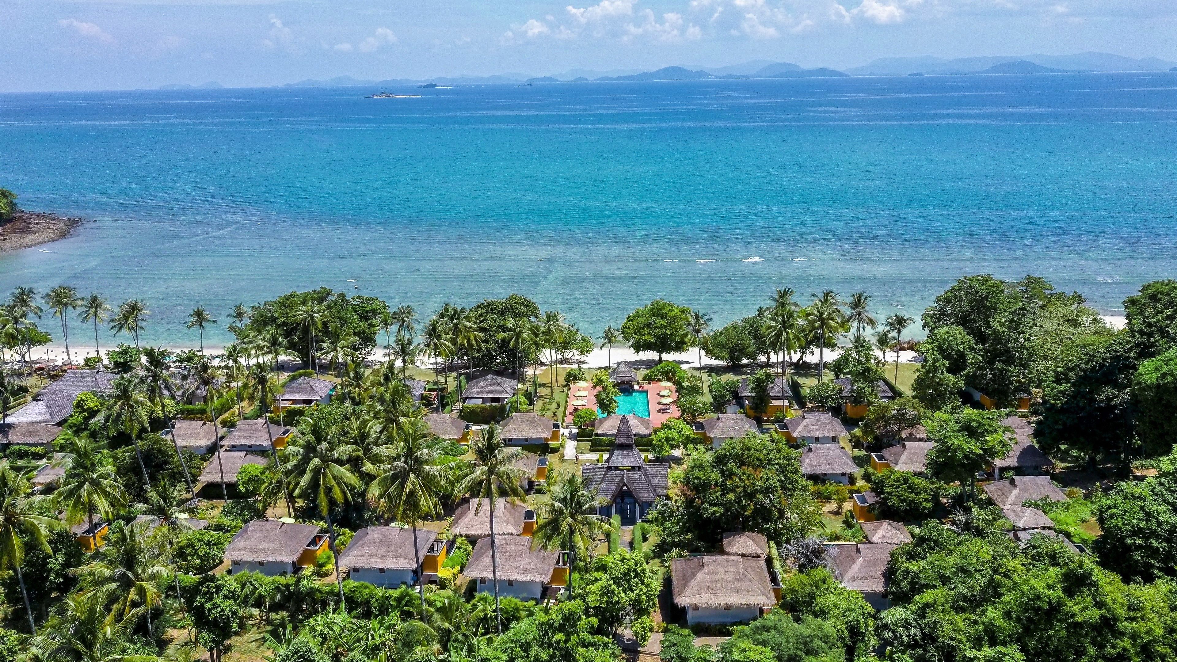 Een resort met rieten bungalows, een zwembad en een strand.