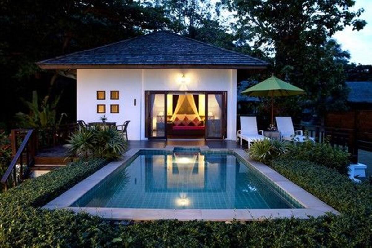 Une maison avec une piscine, un canapé rouge et un parasol vert.