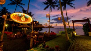 A tiki bar with outdoor seating, palm trees, and a view of the ocean at dusk. - Elixir Koh Yao Yai (Ko Yao)