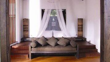 A room with a wooden floor, a sofa with cushions, a canopy bed, and two standing lamps.