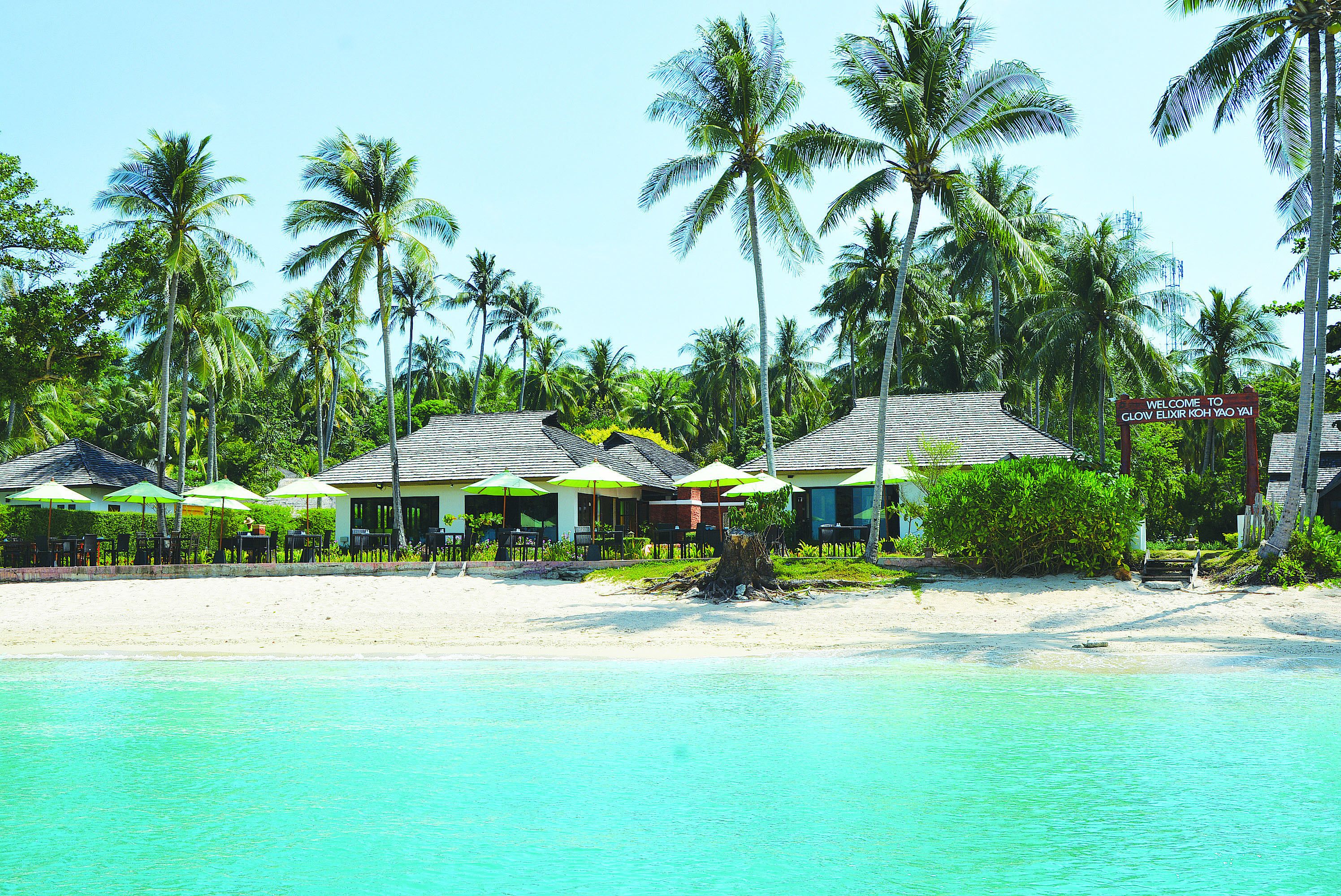 A beach resort with palm trees, beach umbrellas, and a sign welcoming visitors.