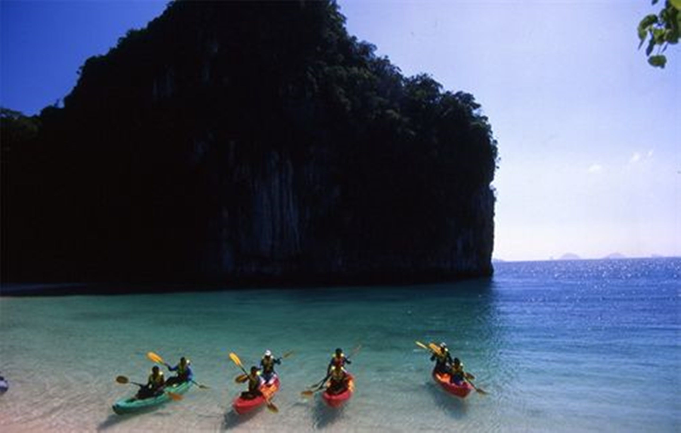 A group of kayakers on a calm sea with a large rock formation in the background.