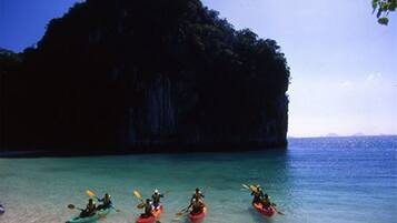 A group of kayakers on a calm sea with a large rock formation in the background.