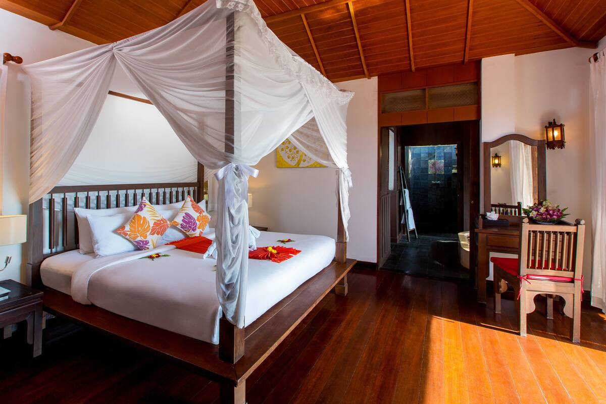 Una cama con dosel, cabecera de madera y almohadas coloridas.