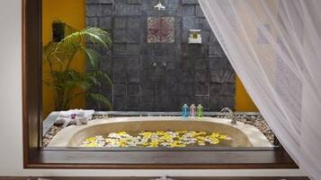 Un baño con una bañera llena de flores, una pared de piedra y una planta en maceta.