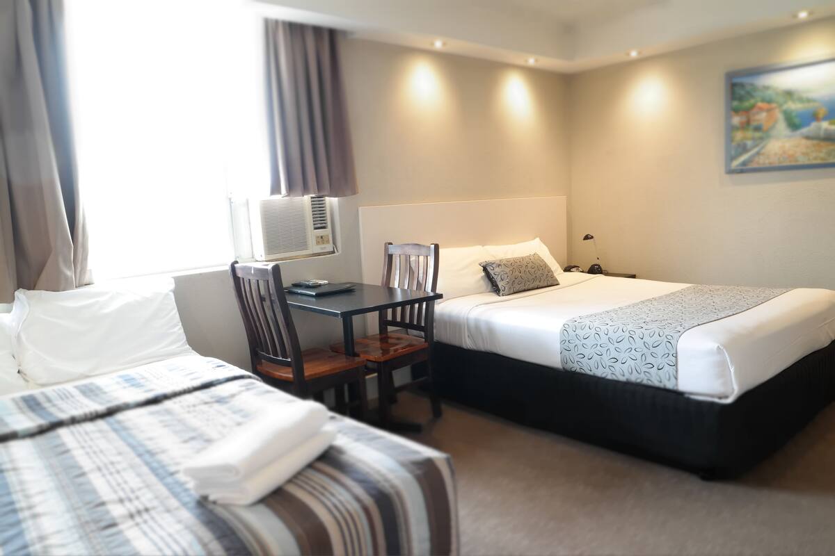 Een hotelkamer met twee bedden, een bureau met stoel, een bureaulamp en een airconditioning.