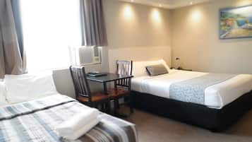 A hotel room with two beds, a desk with a chair, a desk lamp, and an air conditioning unit.