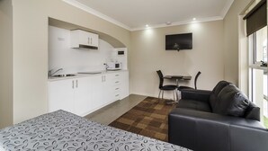 Un espace de vie compact comprenant un coin cuisine, un canapé, une petite table à manger et un téléviseur fixé au mur.