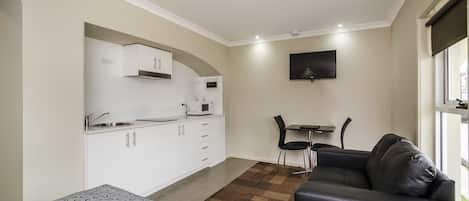 Un espacio habitable compacto con kitchenette, un sofá, una pequeña mesa de comedor y un televisor montado en la pared.