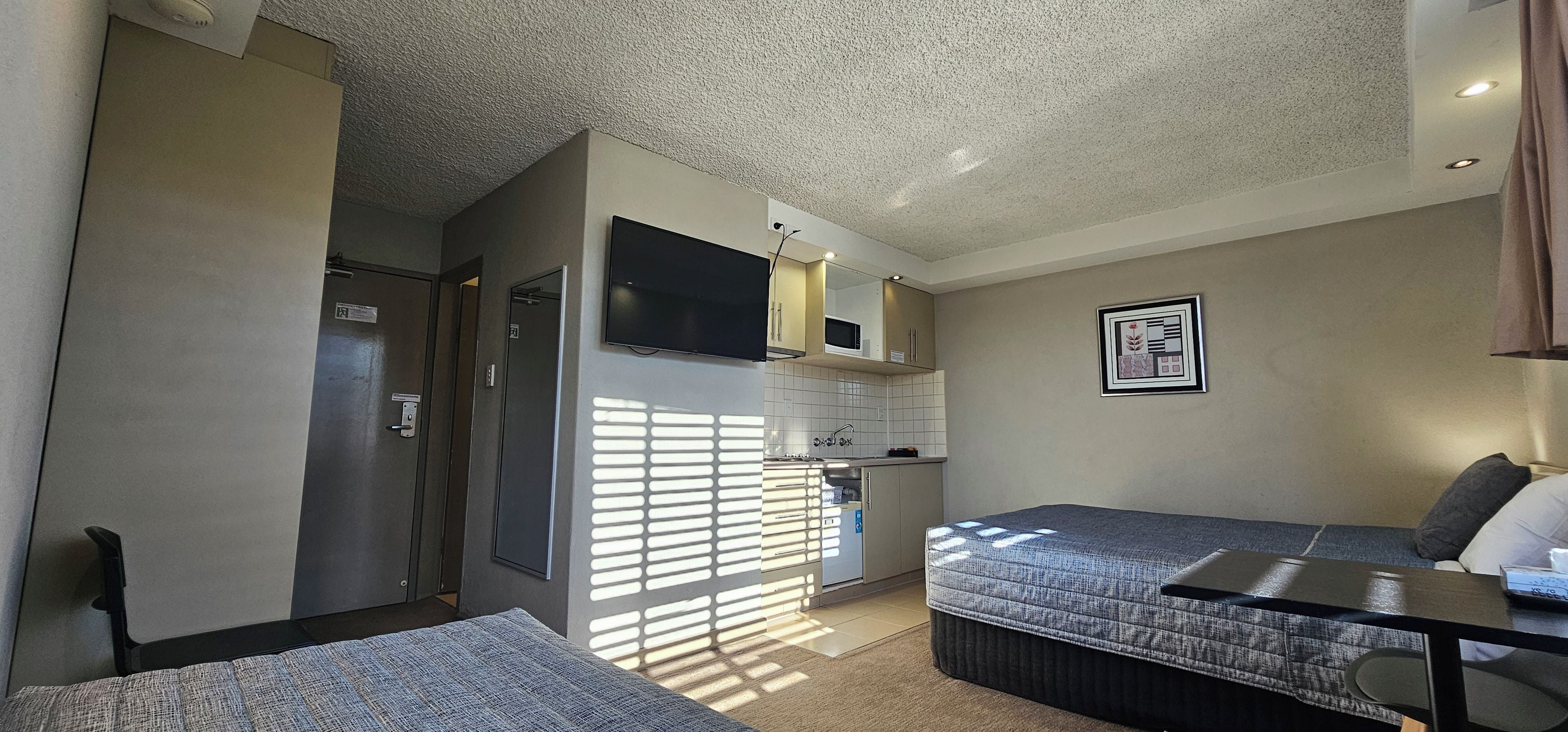 Habitación pequeña con cama, una mesita, kitchenette y zona de ducha.