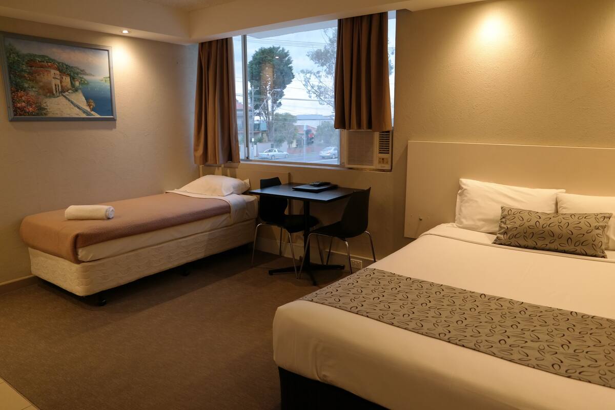 Een hotelkamer met twee bedden, een bureau en een raam met gordijnen.