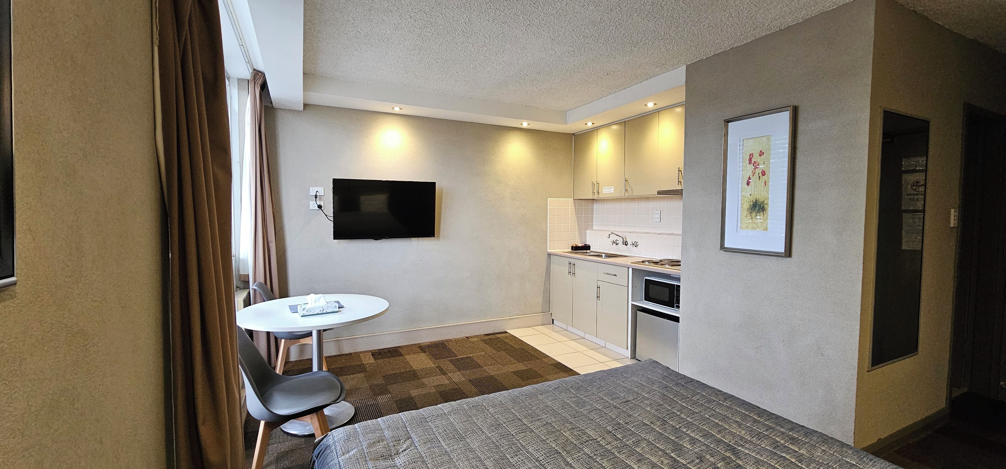 Habitación de hotel compacta con cama, una mesita, televisión, kitchenette y baño.