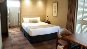 Une chambre d’hôtel équipée d’un lit, d’un bureau, d’une chaise, d’une table de chevet et d’une fenêtre avec des rideaux.