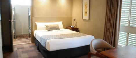 Habitación de hotel con cama, escritorio, silla, mesita de noche y ventana con cortinas.