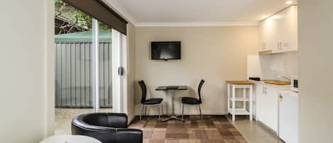 Habitación de hotel compacta con cama, un pequeño escritorio con dos sillas, televisor y kitchenette.