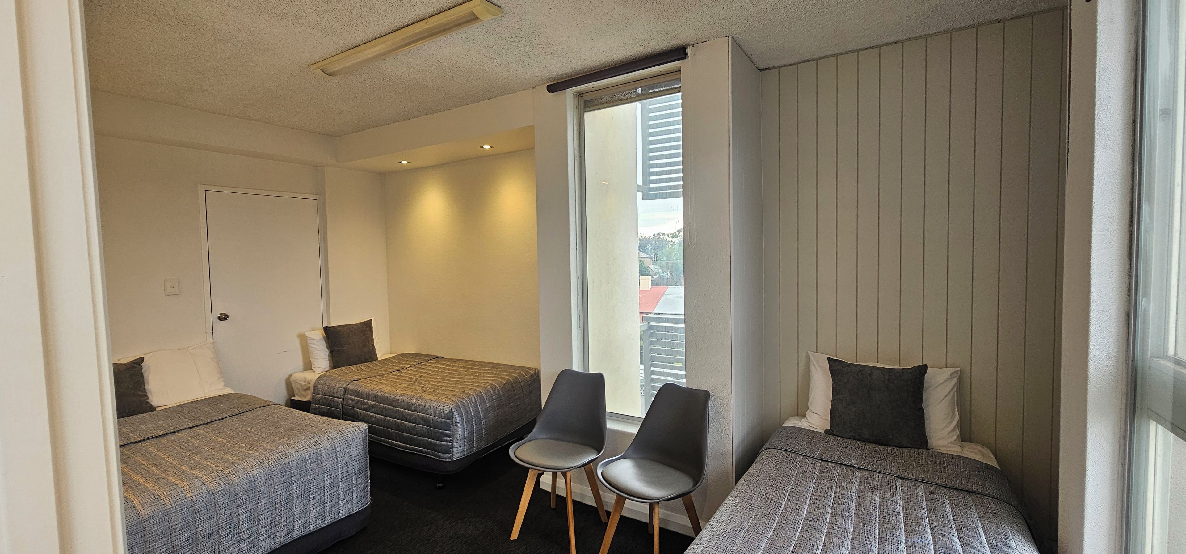 Una habitación con dos camas individuales, una silla y una ventana con vista a edificios.