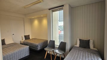 Una habitación con dos camas individuales, una silla y una ventana con vista a edificios.