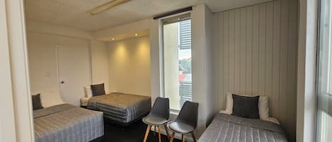 Una habitación con dos camas individuales, una silla y una ventana con vista a edificios.