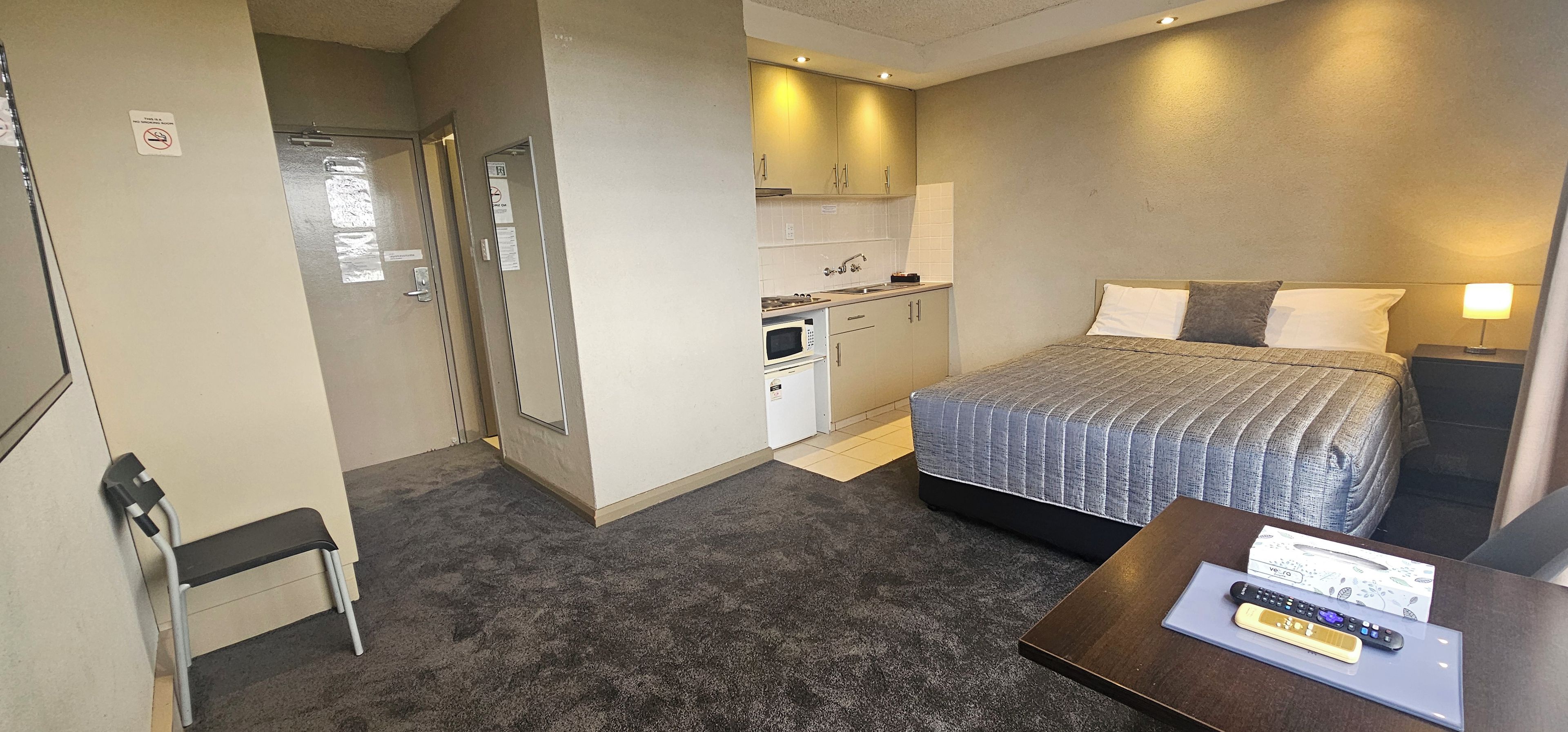 Una habitación de hotel compacta con una cama, una kitchenette pequeña, un escritorio y una silla.