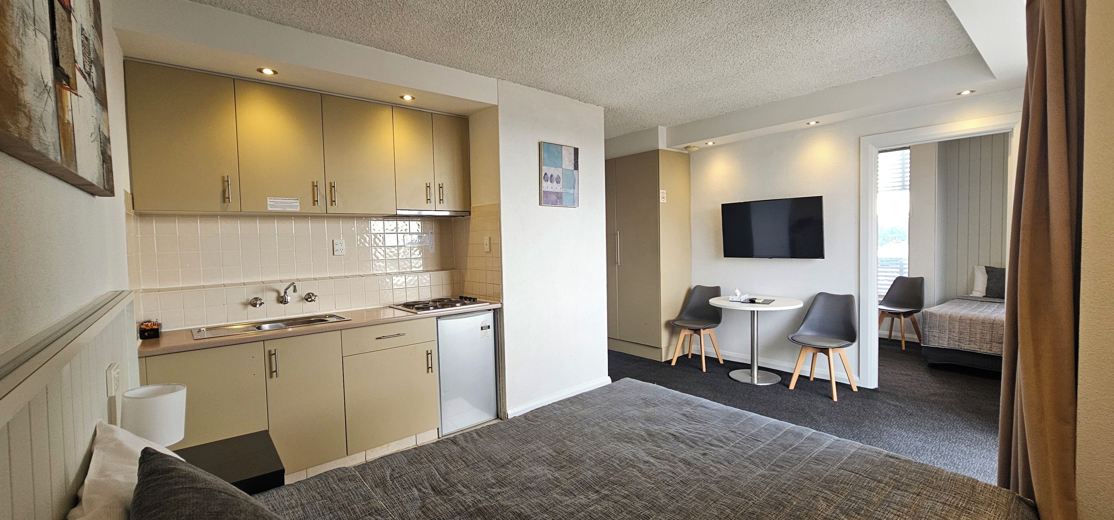 Una habitación de hotel compacta con kitchenette, zona de comedor, televisor y cama.