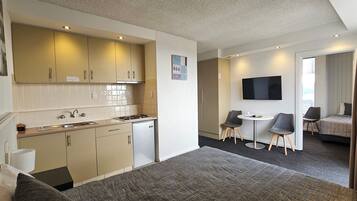 Una habitación de hotel compacta con kitchenette, zona de comedor, televisor y cama.