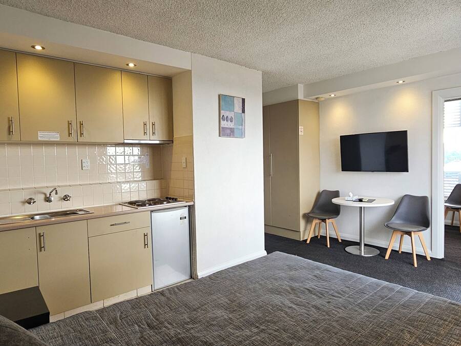 Una habitación de hotel compacta con kitchenette, zona de comedor, televisor y cama.