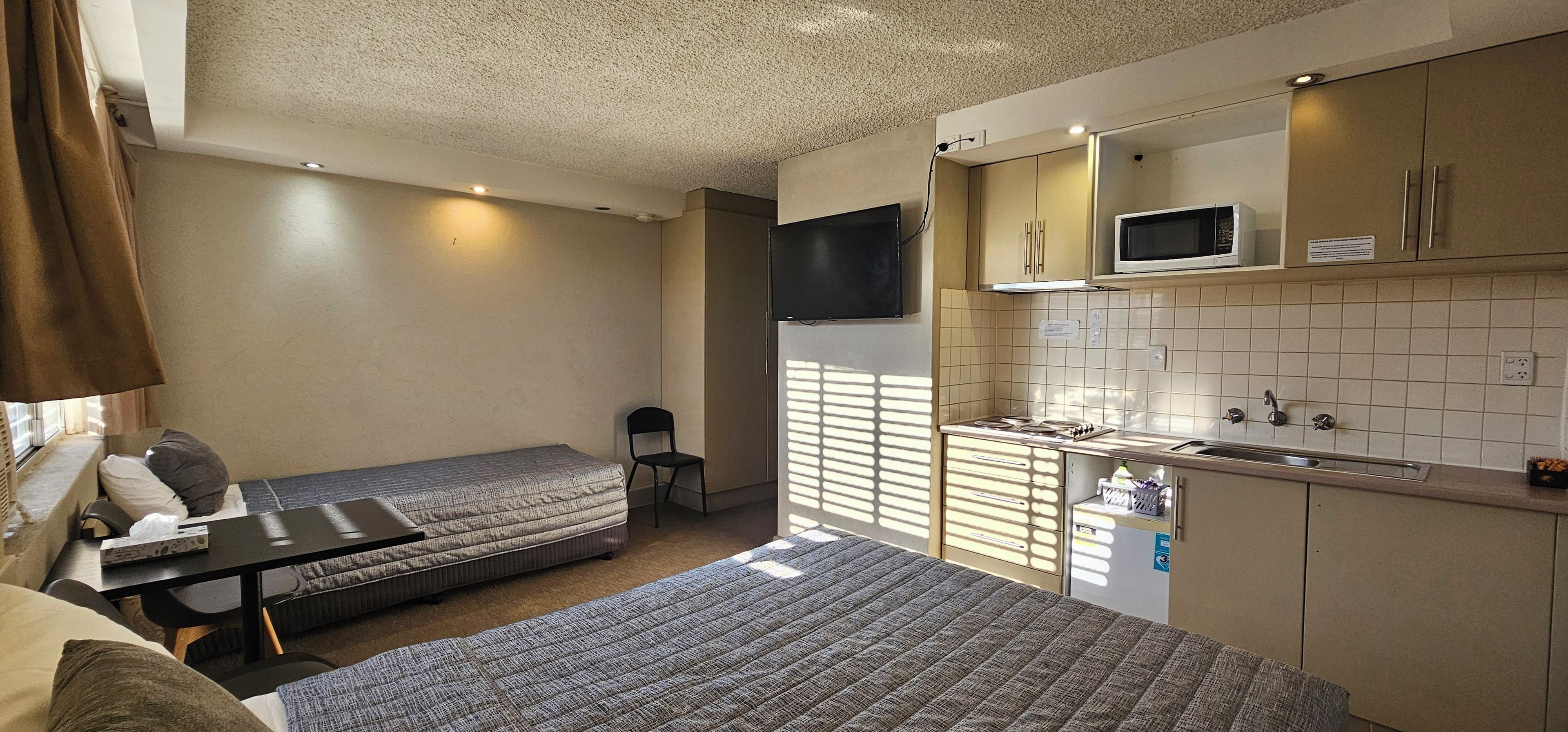 Habitación de hotel compacta con kitchenette, una cama, una mesita y una silla.