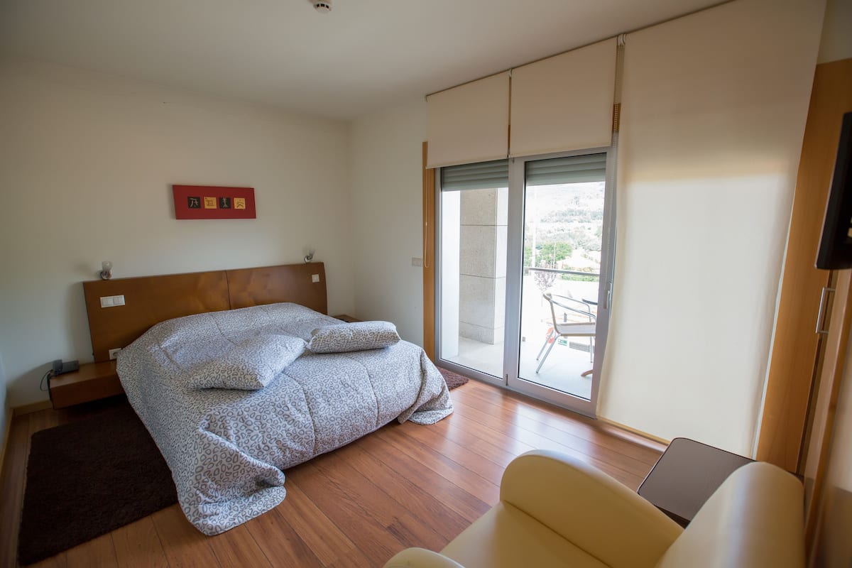 A bedroom with a bed, a sofa, a sliding glass door to a balcony, and a red sign on the wall.