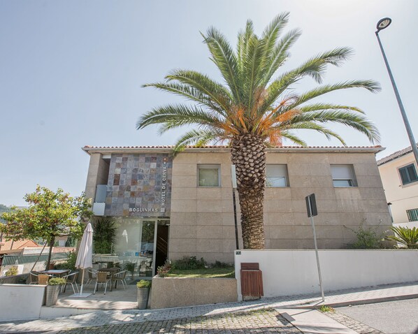 Un hôtel avec une façade recouverte de carreaux, des places assises à l’extérieur et un palmier.