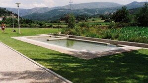 A rectangular pool with a paved border, surrounded by well-maintained grass, set against a backdrop of rolling hills and distant mountains.