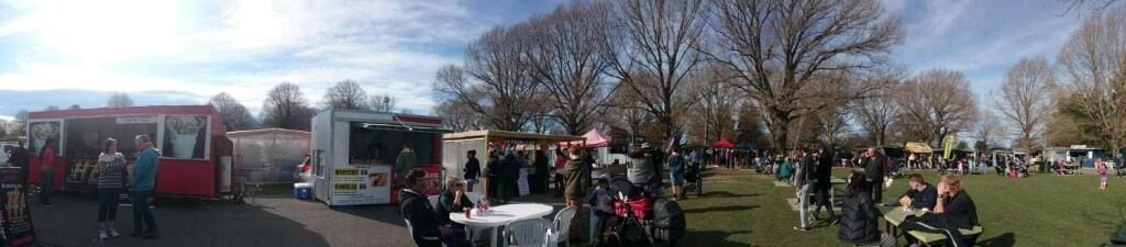 A park with food trucks and people sitting on the grass.