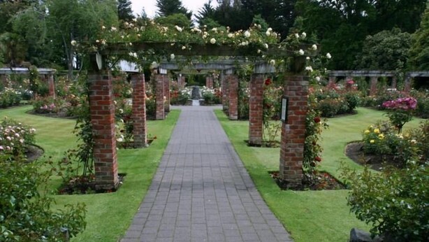 Un sendero de jardín con pilares de ladrillo y un arco de ladrillo cubierto de flores.