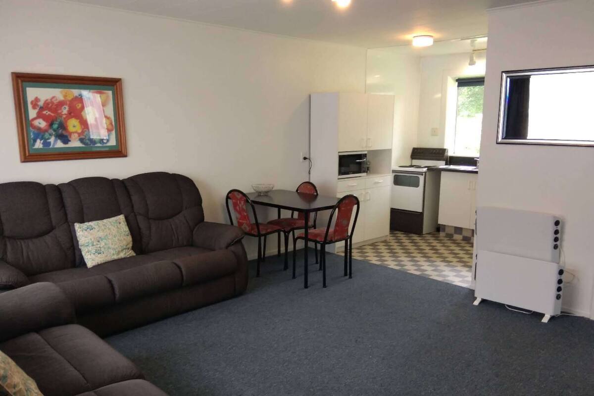 A compact living space with a sofa, a dining table with chairs, a kitchenette, and a refrigerator.