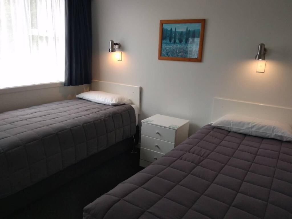 A room with two beds, a nightstand, and a wall-mounted light fixture.