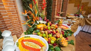 En buffetbord med et udvalg af frugt og grøntsager, herunder æbler, bananer og gulerødder, anrettet i et dekorativt mønster.